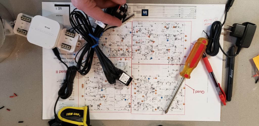 A top-down photograph of a detailed schematic on a table, with a screwdriver and bundle of wires on top